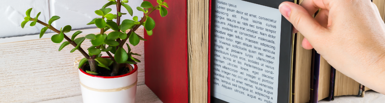 May Discover New Books 2025 banner image A hand holding an e-reader next to a red book and a small potted plant on a wooden surface, with text visible on the e-reader screen.