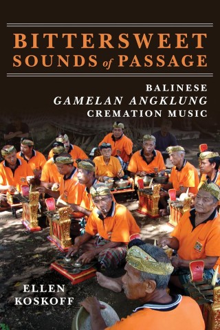 Group of Balinese musicians in orange shirts and traditional headwear play Gamelan Angklung instruments in a shaded outdoor setting, conveying cultural vibrancy.