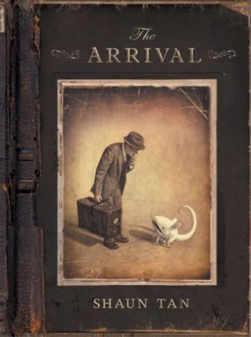 Cover of "The Arrival" by Shaun Tan. A sepia-toned image shows a man in a hat and suit, holding a suitcase, curiously facing a small, white creature.