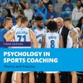 A basketball coach passionately talks to his team during a game, with cheering fans holding blue banners in the background. Cover of "Psychology in Sports Coaching" by Adam R. Nicholls.