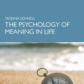 A book cover featuring a blue background with the title "The Psychology of Meaning in Life" by Tatjana Schnell. Foreground shows a compass on a sandy beach.